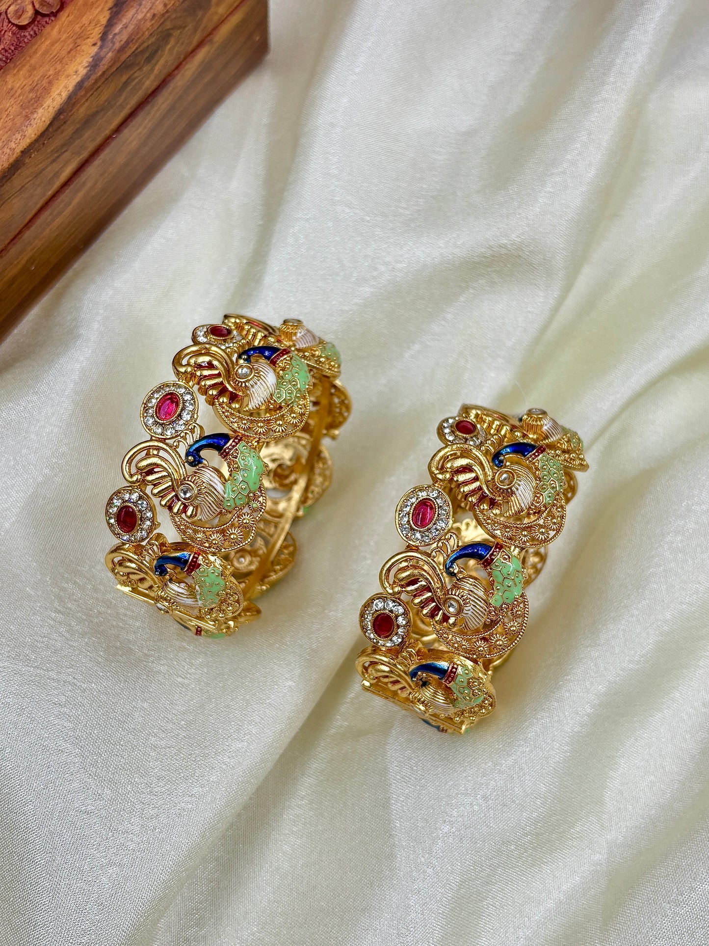Gold earrings with colorful gemstones on a white fabric background by hitesh bangles
