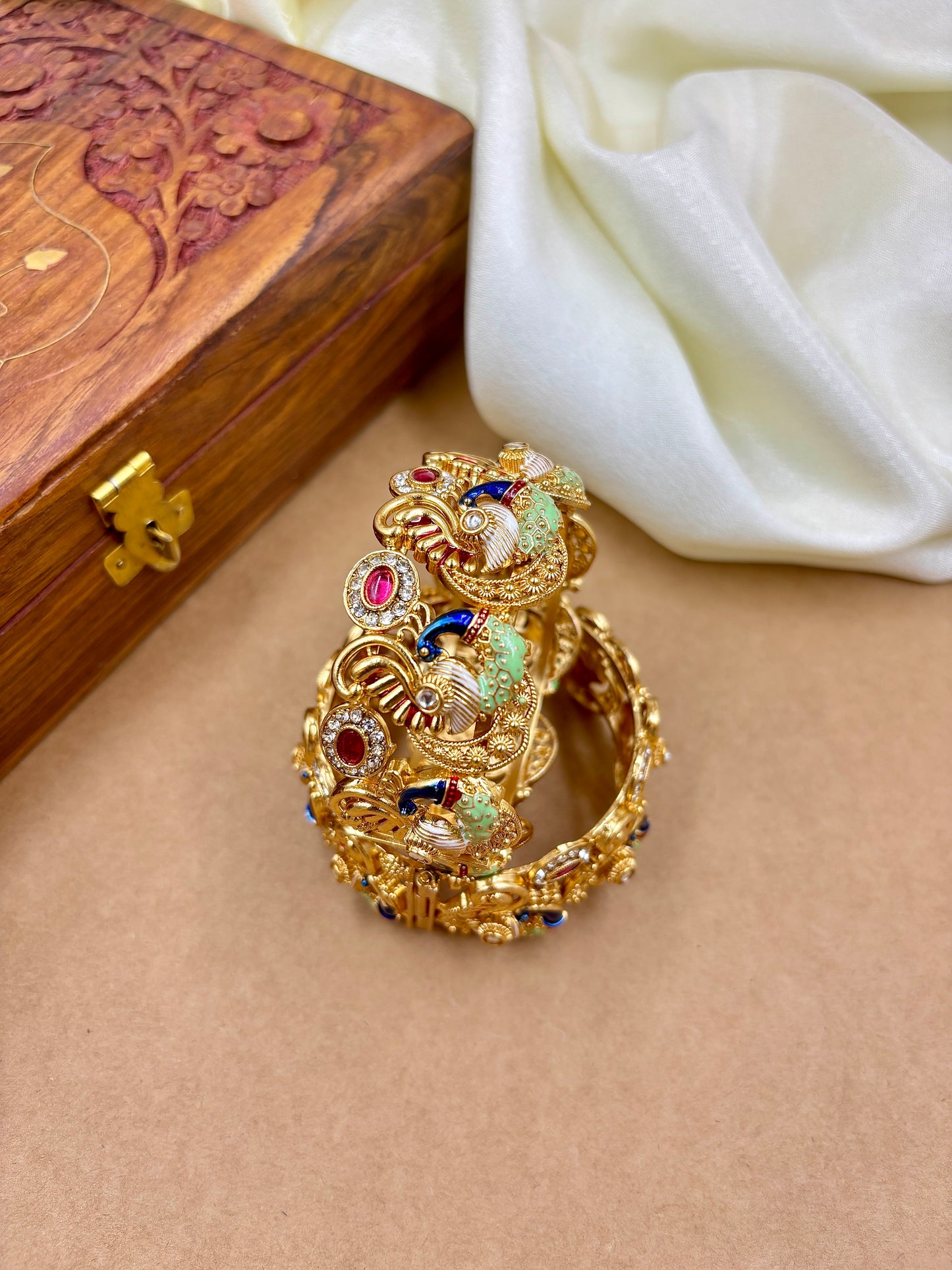 Gold ring with colorful gemstones on a beige surface with a wooden box in the background by hitesh bangles