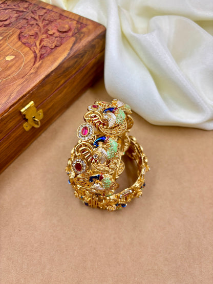 Gold ring with colorful gemstones on a beige surface with a wooden box in the background by hitesh bangles