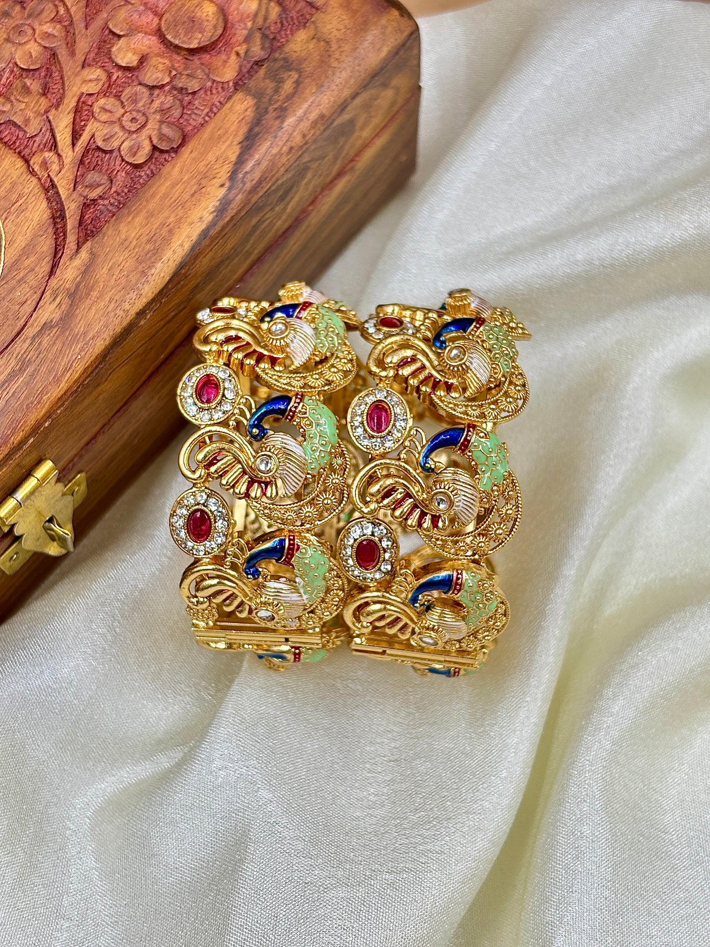 Decorative gold brooch with gemstones on a wooden box and white fabric background by hitesh bangles