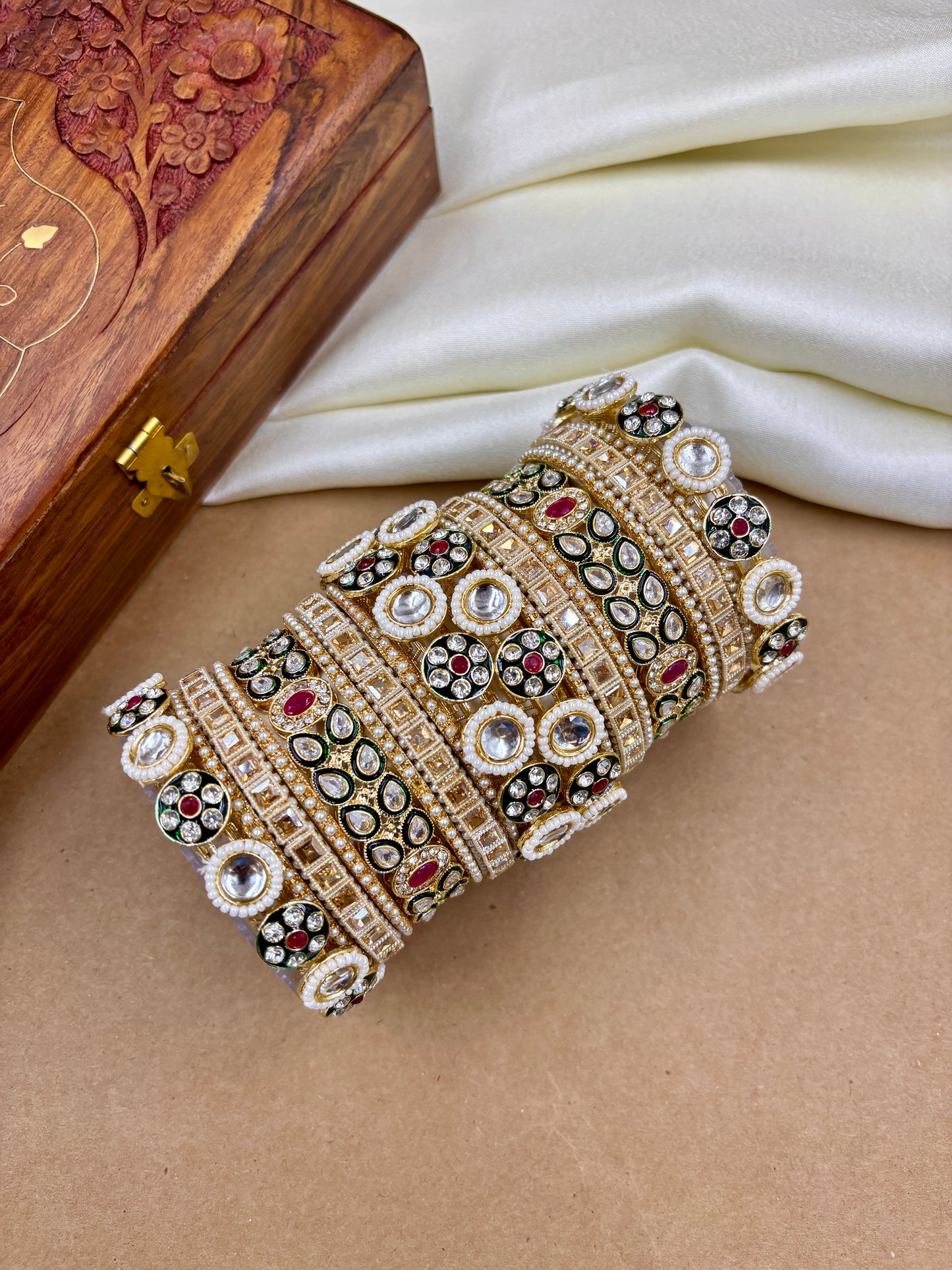 Decorative bracelet with gemstones on a beige surface with a wooden box in the background by hitesh bangles