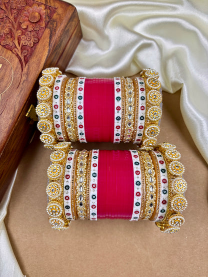 Pair of ornate bangles with red center and gold, red, and white patterns on a beige surface by hitesh bangles