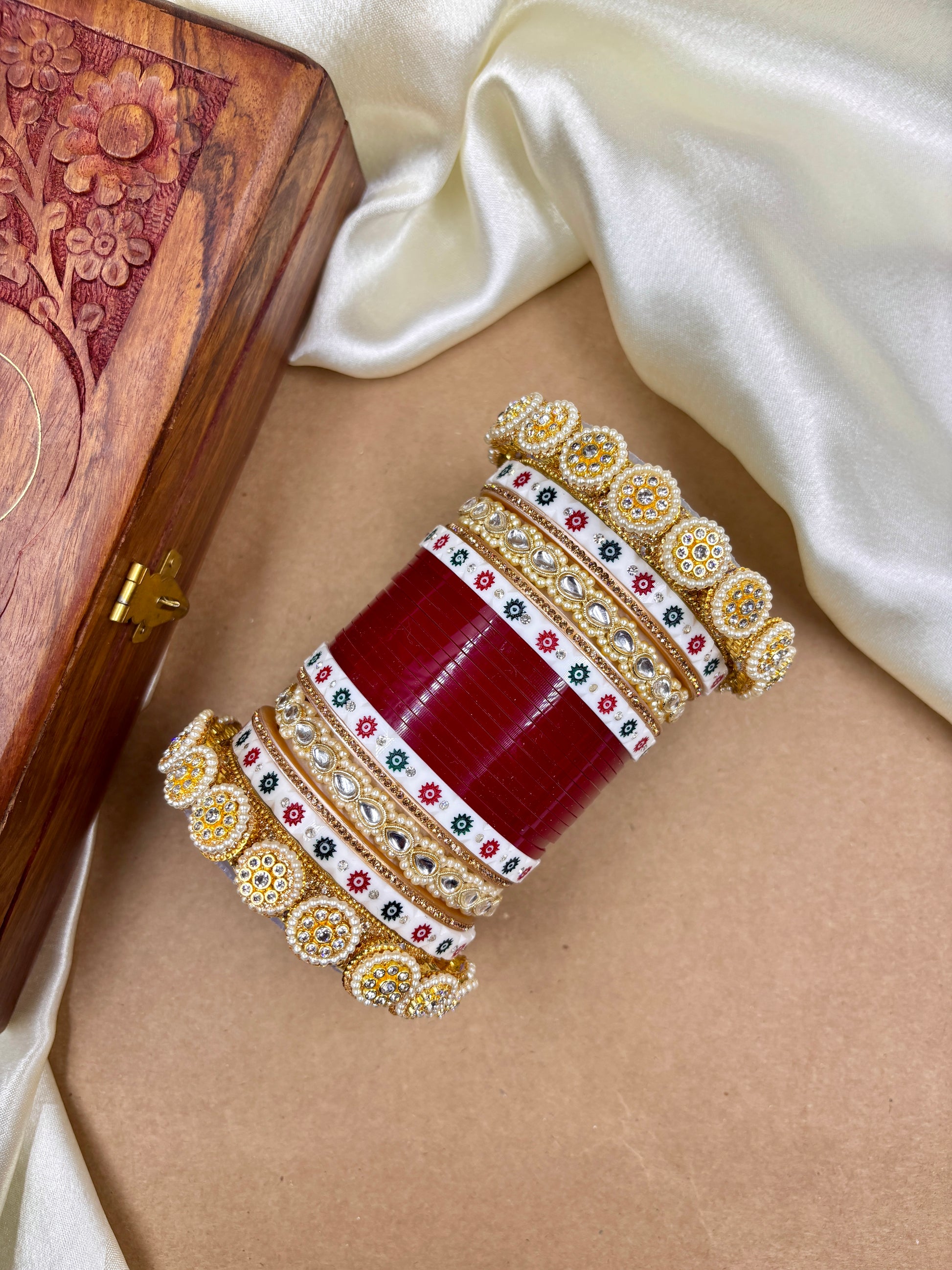 Decorative red and gold bangles on a beige surface with a wooden box in the background by hitesh bangles