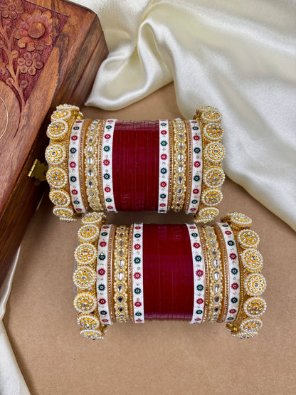 Pair of red and gold bangles with intricate designs on a beige surface by hitesh bangles
