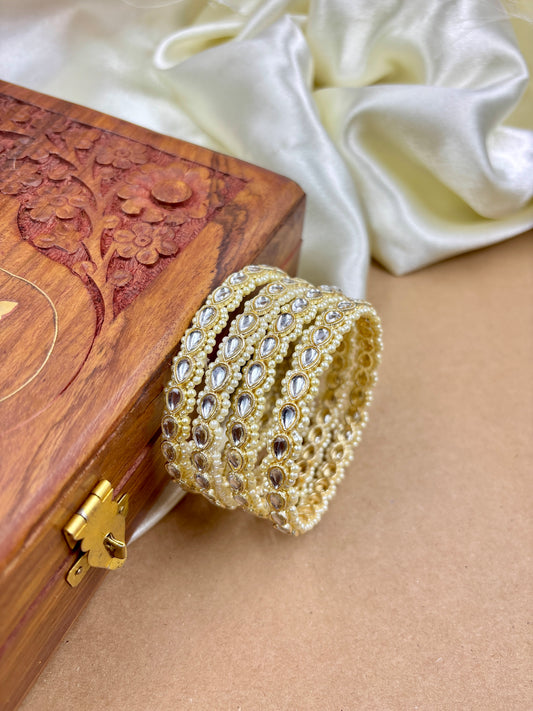 Gold bracelet with intricate design on a wooden box and white fabric background by hitesh bangles