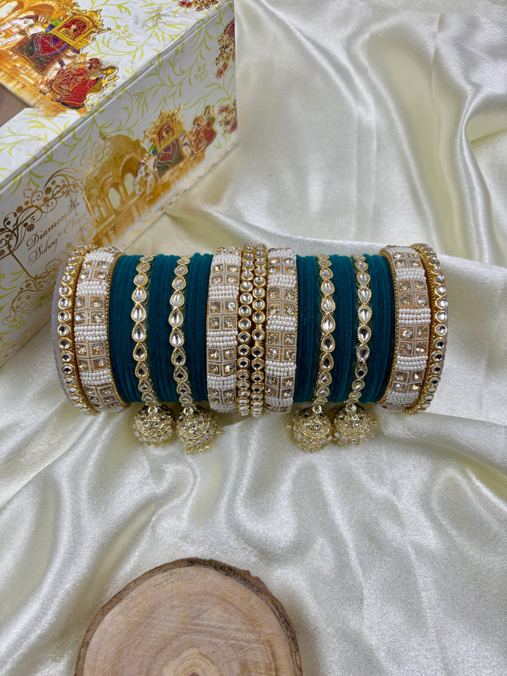 Sapphire green and gold bridal chura set featuring intricate kundan stonework, velvet bangles, and traditional pearl hangings, displayed on a satin background.