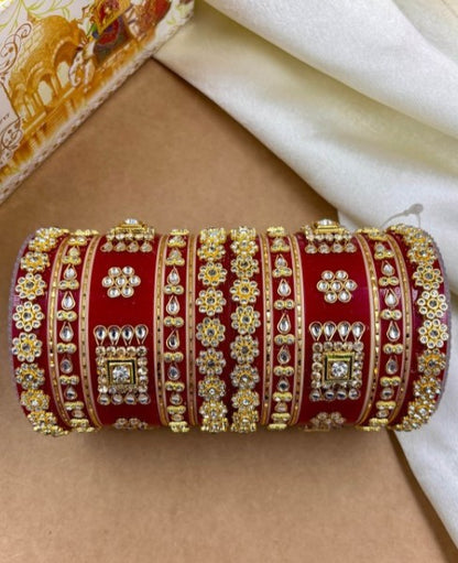Decorative red and gold bangle on a beige surface with a white fabric background by hitesh bangles