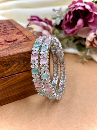 Two decorative bracelets with gemstones on a wooden surface with flowers in the background by hitesh bangles