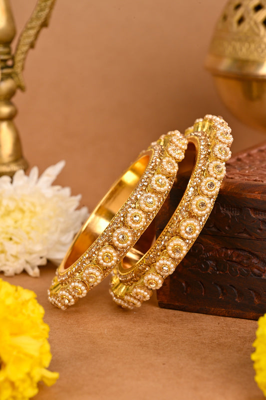 Gold bangles with intricate designs on a decorative background with flowers and pots. by hitesh bangles