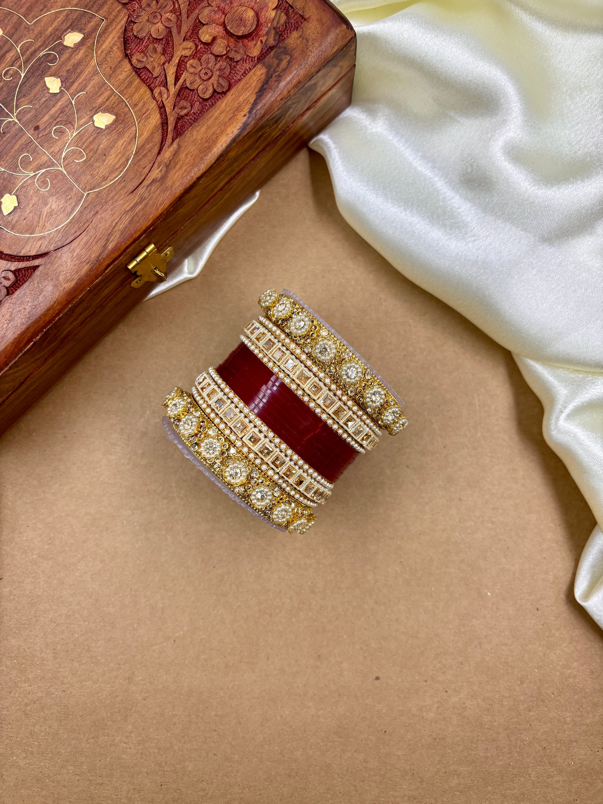 Decorative ring with red stone and gold accents on a beige surface, next to a wooden jewelry box by hitesh bangles