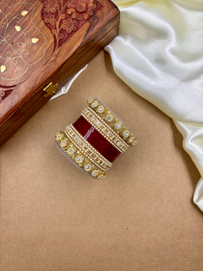 Decorative ring with red stone and gold accents on a beige surface, next to a wooden jewelry box by hitesh bangles