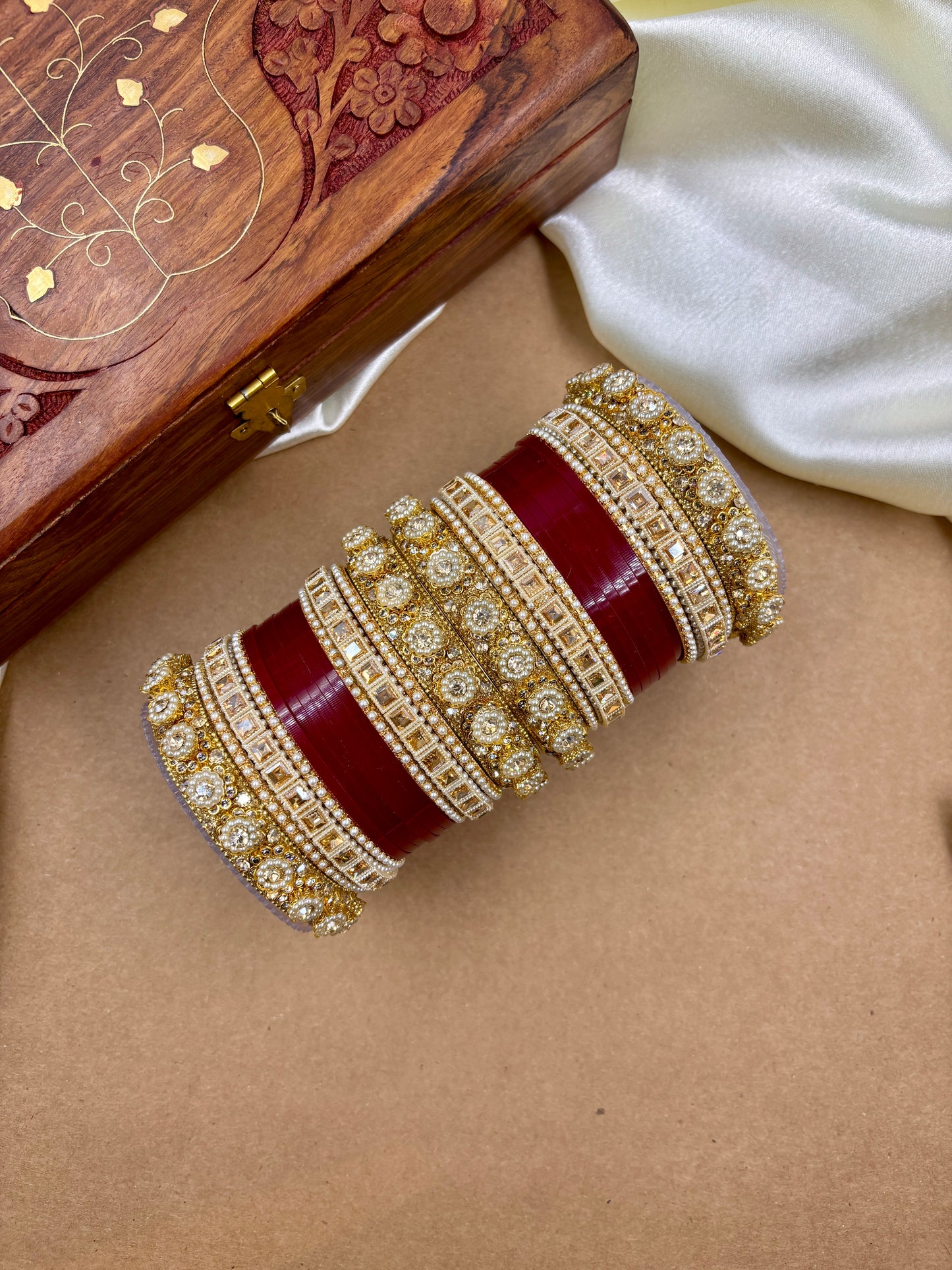 Decorative red and gold bracelet on a beige surface with a wooden box in the background by hitesh bangles