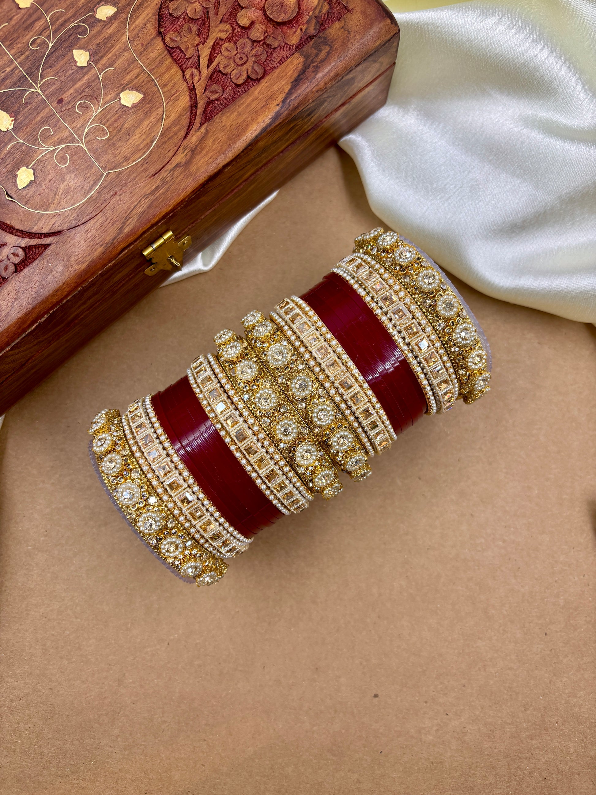 Decorative red and gold bracelet on a beige surface with a wooden box in the background by hitesh bangles
