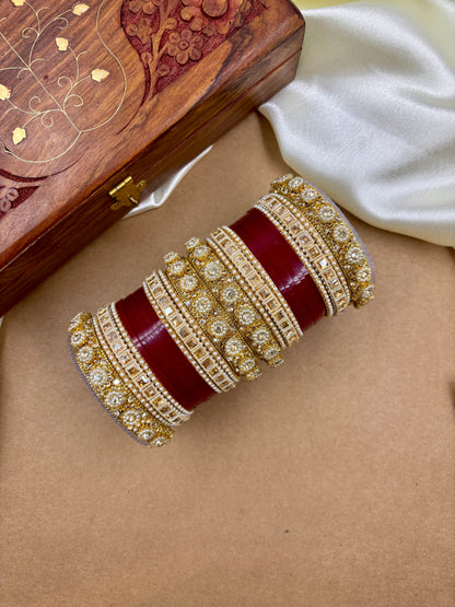 Decorative red and gold bracelet on a beige surface with a wooden box in the background by hitesh bangles
