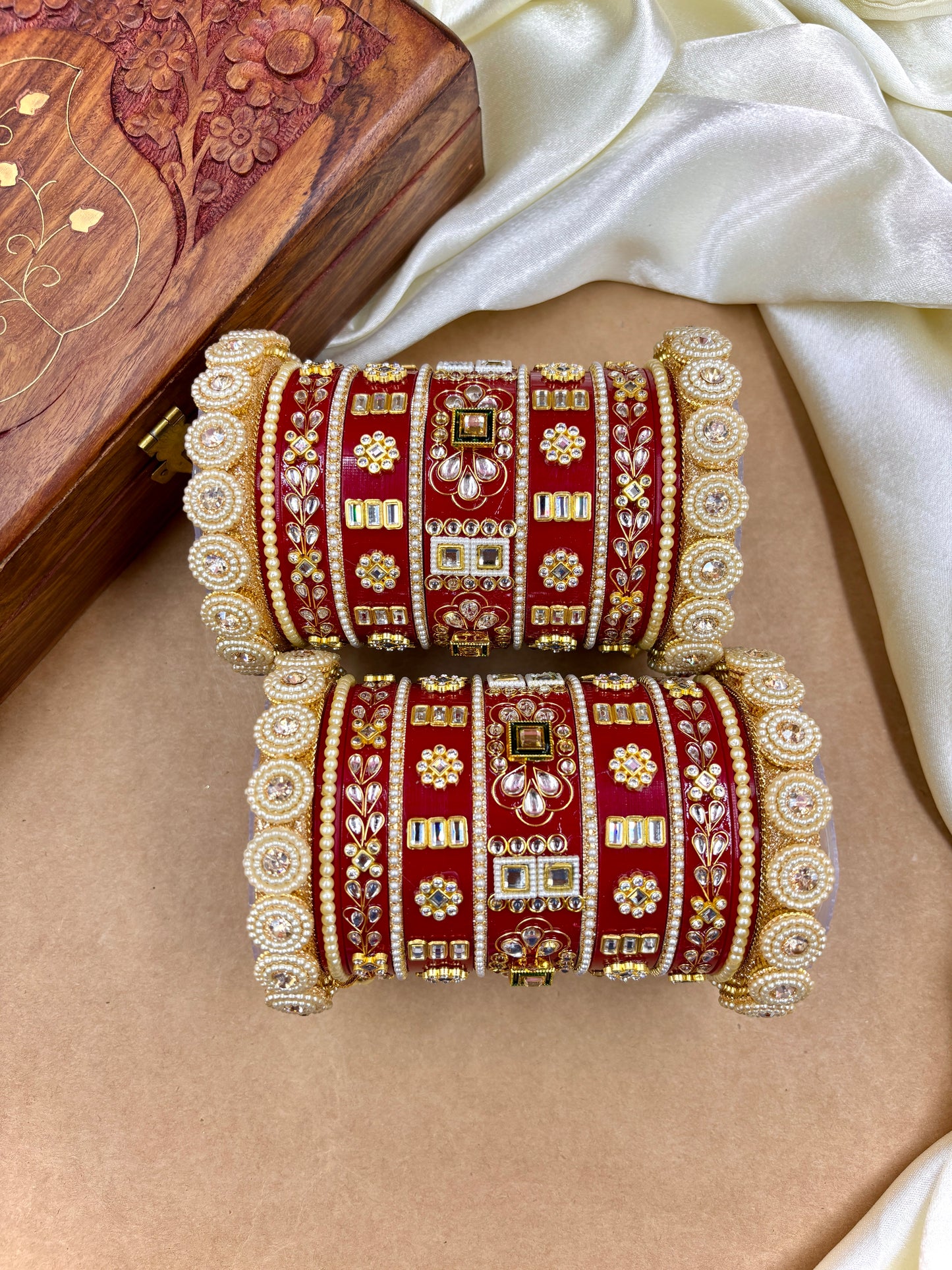 Pair of red and gold bangles with intricate designs on a beige surface by hitesh bangles