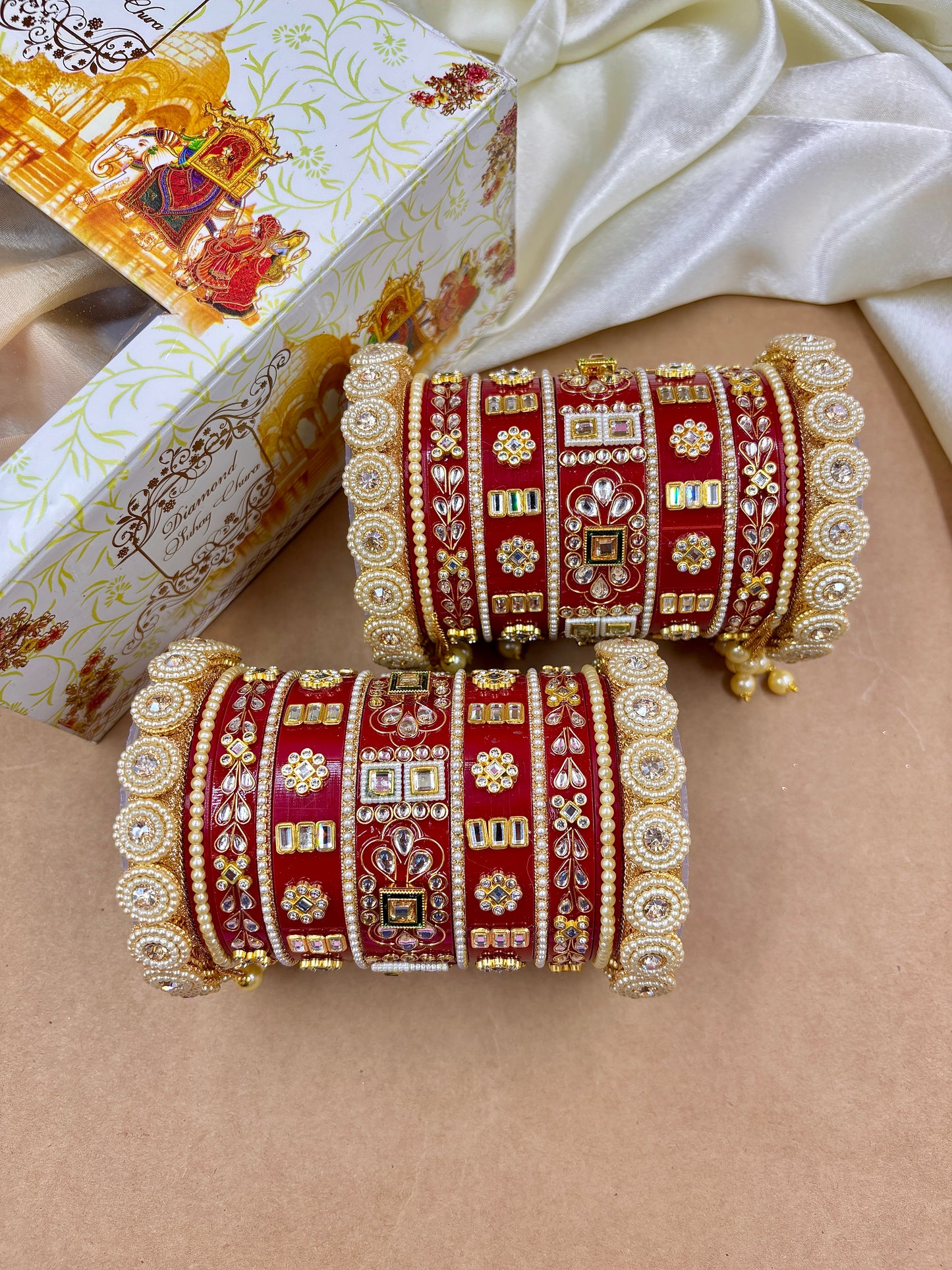 Decorative red and gold bangles on a beige surface with a decorative box in the background by hitesh bangles