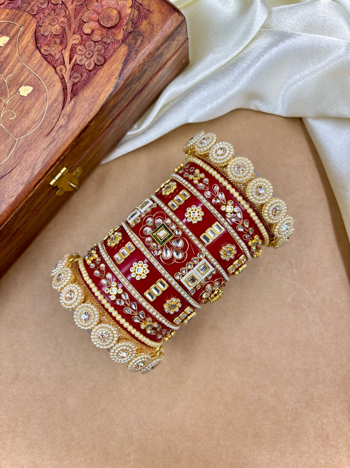 Decorative red and gold bracelet on a person's wrist with a wooden box in the background by hitesh bangles
