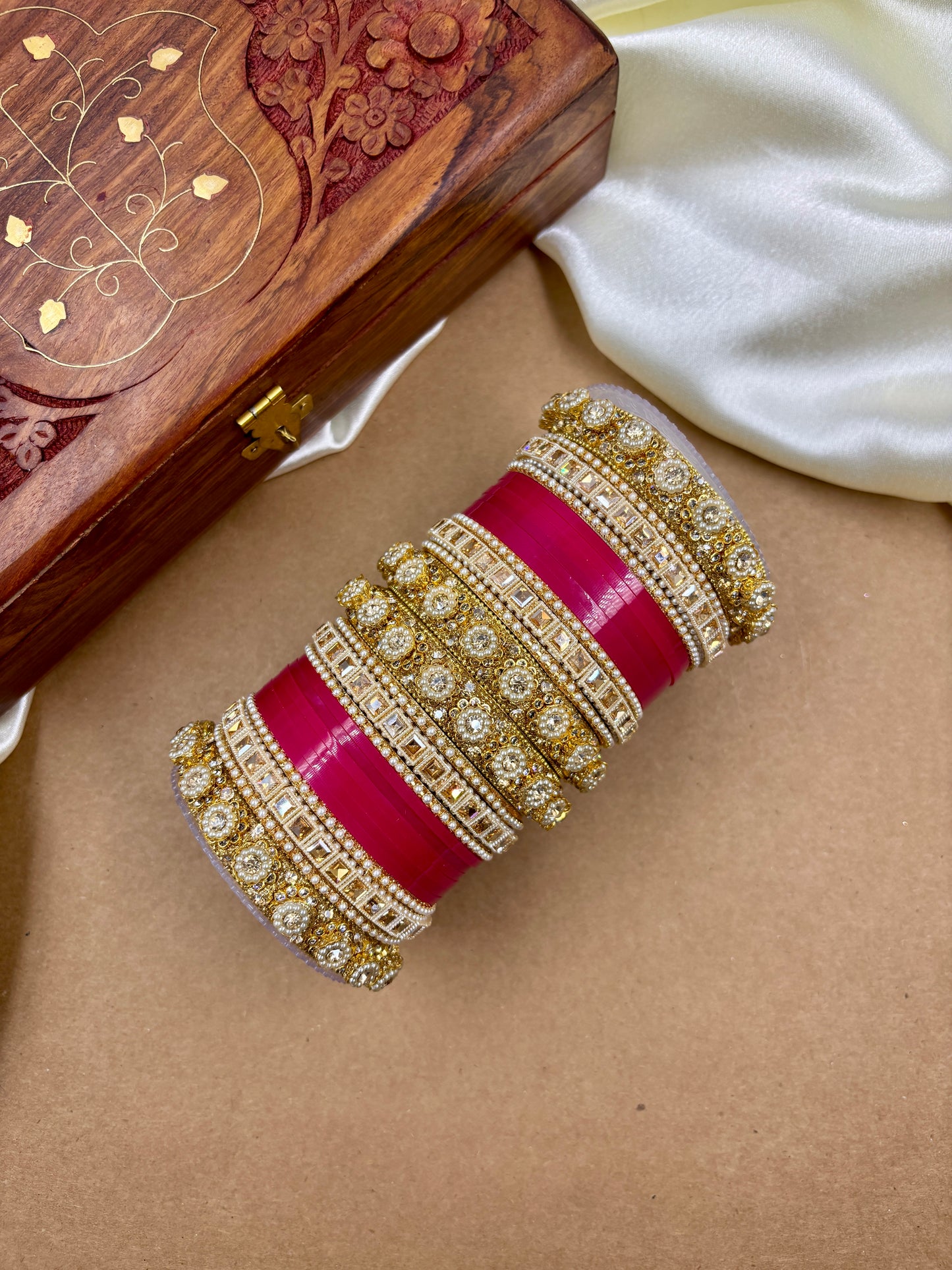 Decorative red and gold bangle on a beige surface with a wooden box in the background by hitesh bangles