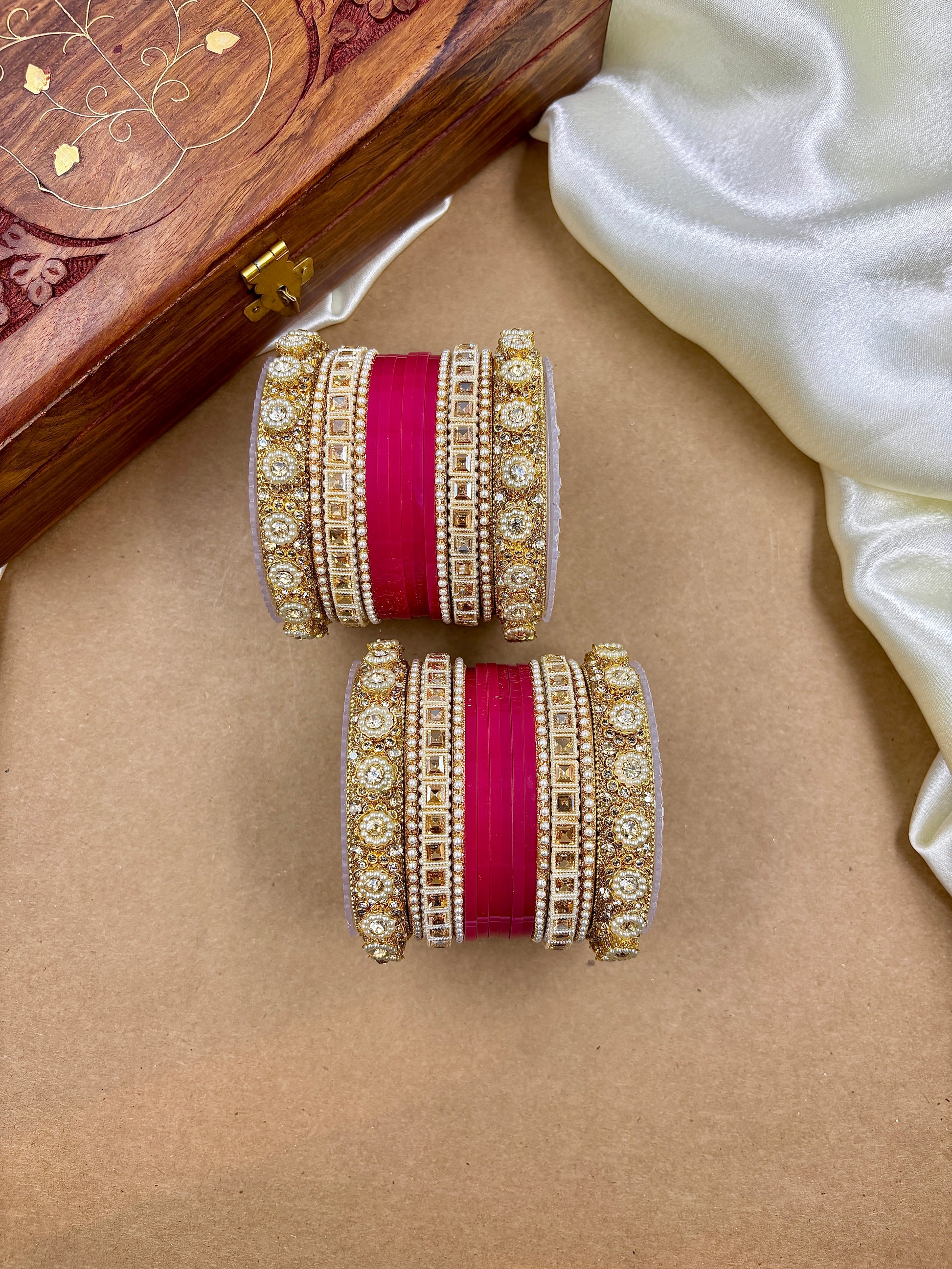 Decorative bangles with red ribbons on a beige surface, with a wooden box and white fabric in the background by hitesh bangles
