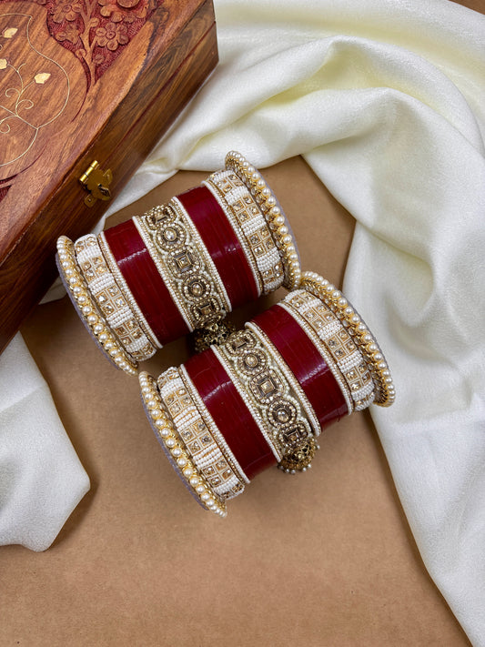 Decorative red and gold bangles on a beige surface with a white fabric background by hitesh bangles