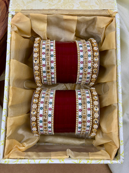 Pair of ornate bangles with red center and gold, silver, and gemstone accents in a decorative box by hitesh bangles