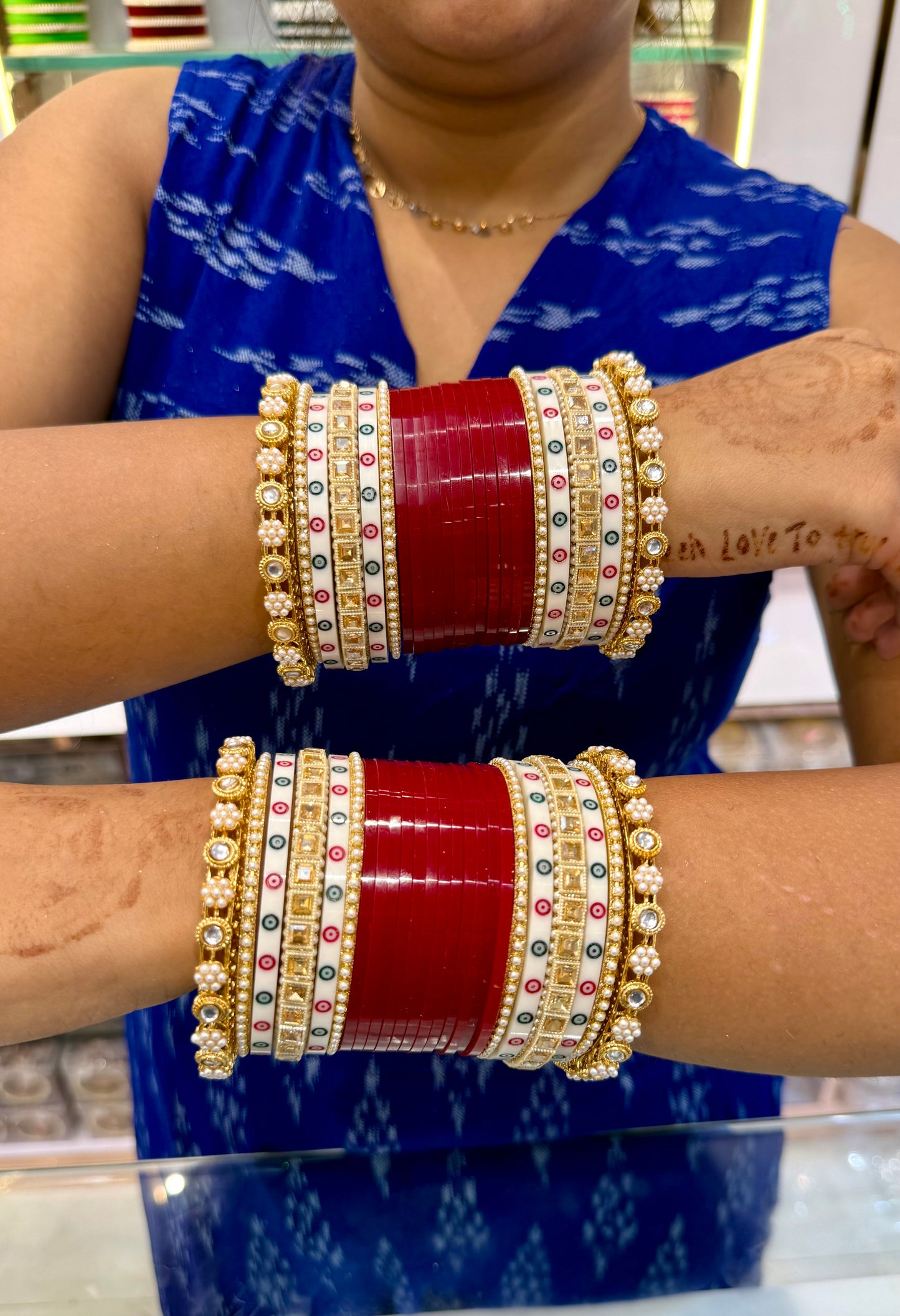 Person wearing red and gold bangles on both wrists with a blue sleeve by hitesh bangles