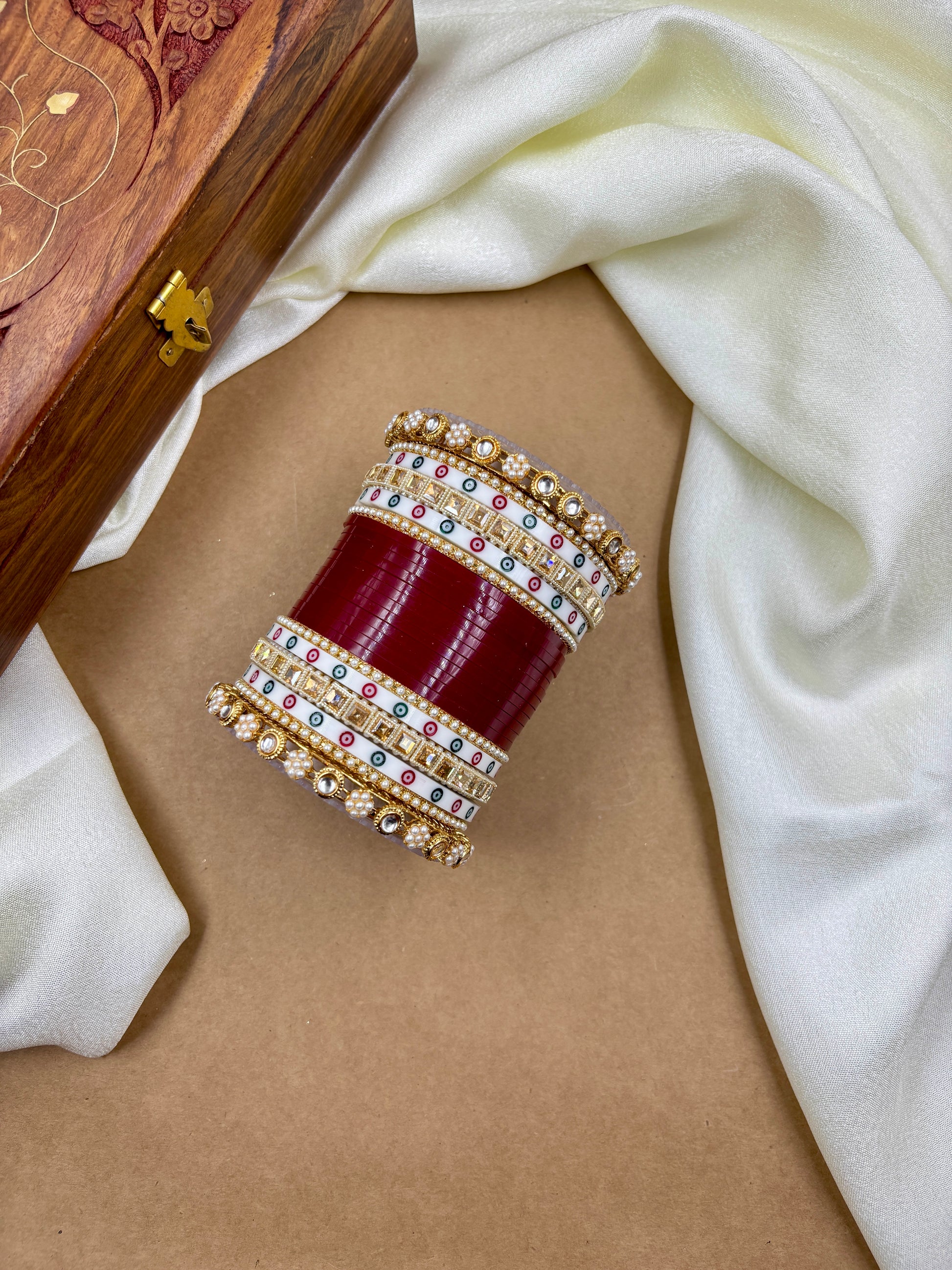 Decorative bangles with red and gold accents on a beige surface with white fabric by hitesh bangles