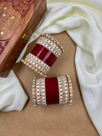 Pair of red and gold bangles with gemstones on a beige surface with a white fabric background by hitesh bangles