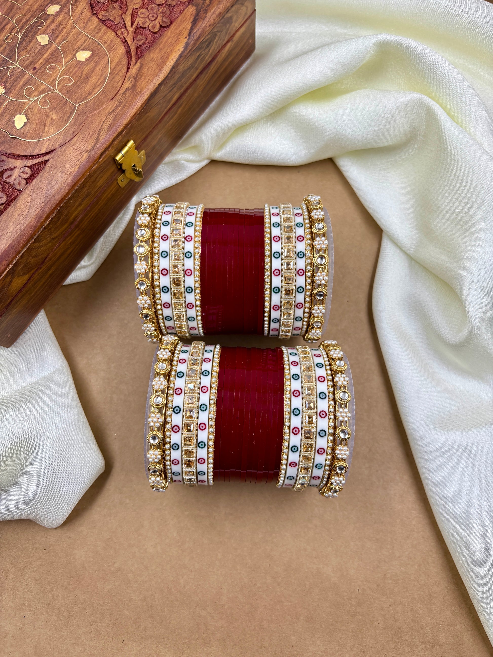 Decorative bangles with colorful stones on a beige surface, with a wooden box in the background by hitesh bangles