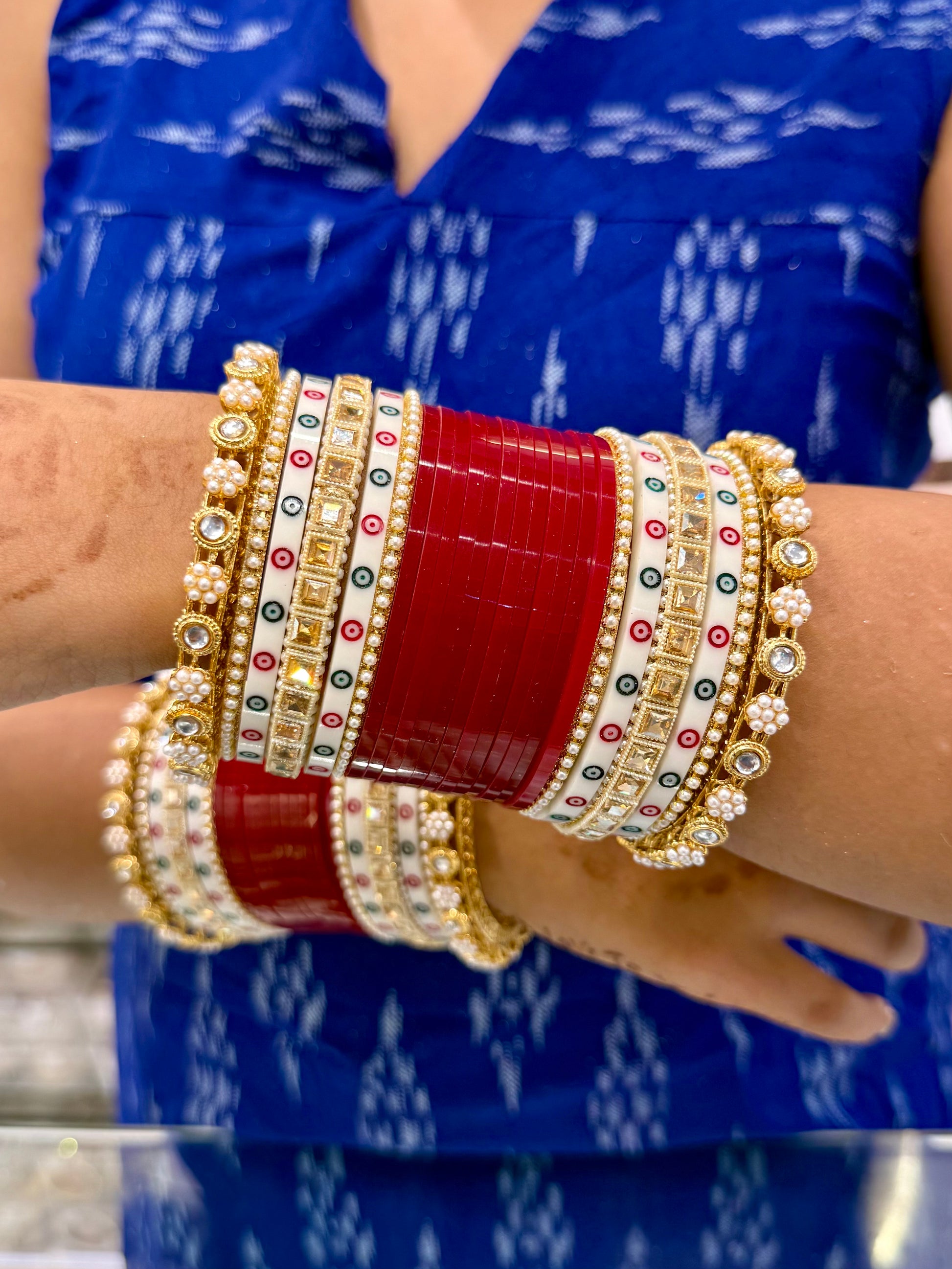 Close-up of a hand wearing multiple colorful bangles on a blue patterned fabric background by hitesh bangles