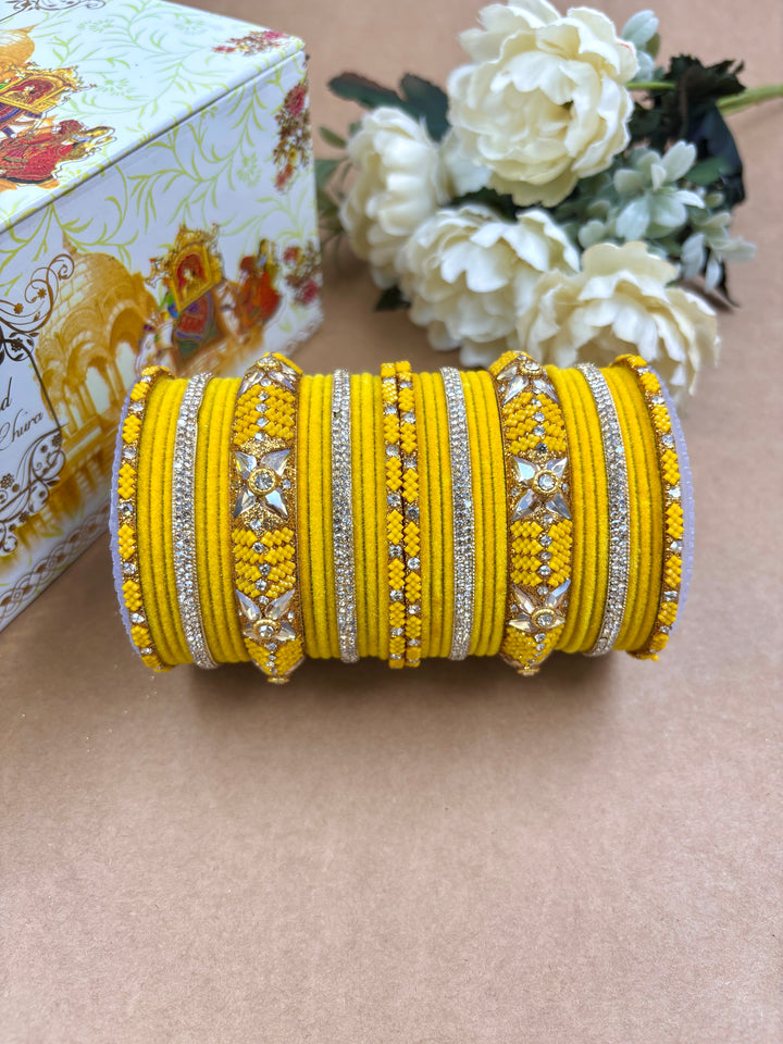"Vibrant yellow metal velvet bangle set for women adorned with American diamonds and floral motifs, ideal for weddings and festive occasions by Hitesh Bangles."