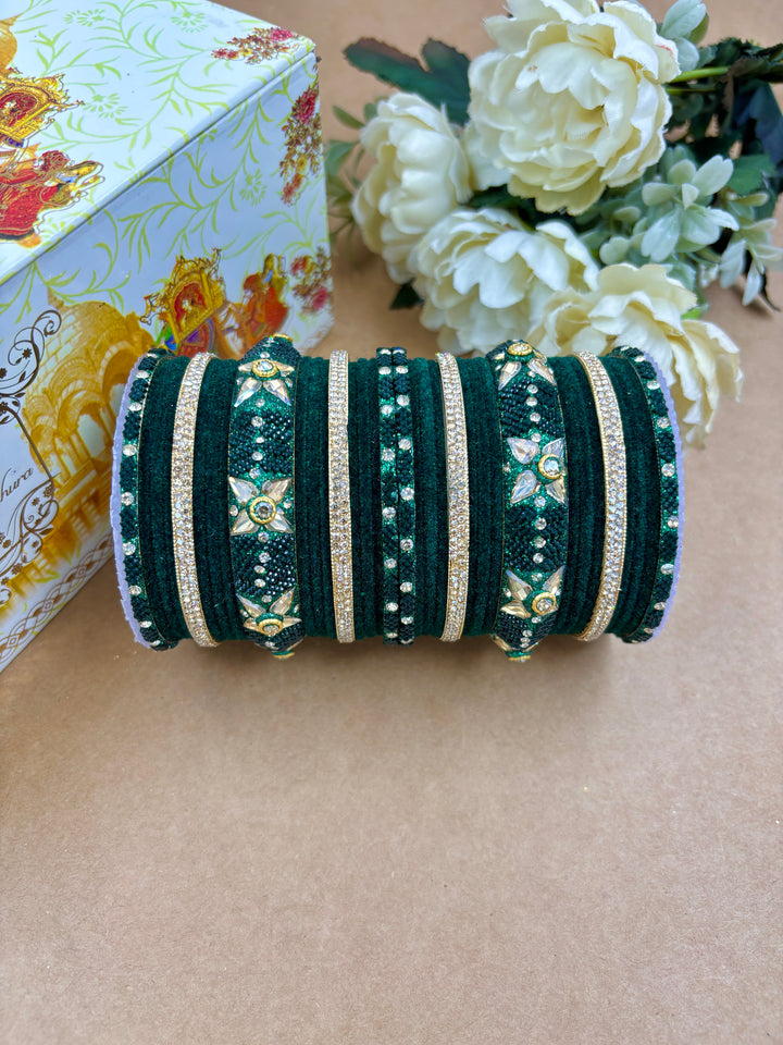 Emerald green velvet metal bridal bangle set featuring gold accents, kundan floral motifs, and shimmering stonework, styled with floral decor and a designer box.
