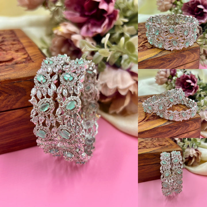 Elegant turquoise American diamond kada bangles with intricate silver detailing and sparkling stone embellishments, placed on a wooden box with floral background.