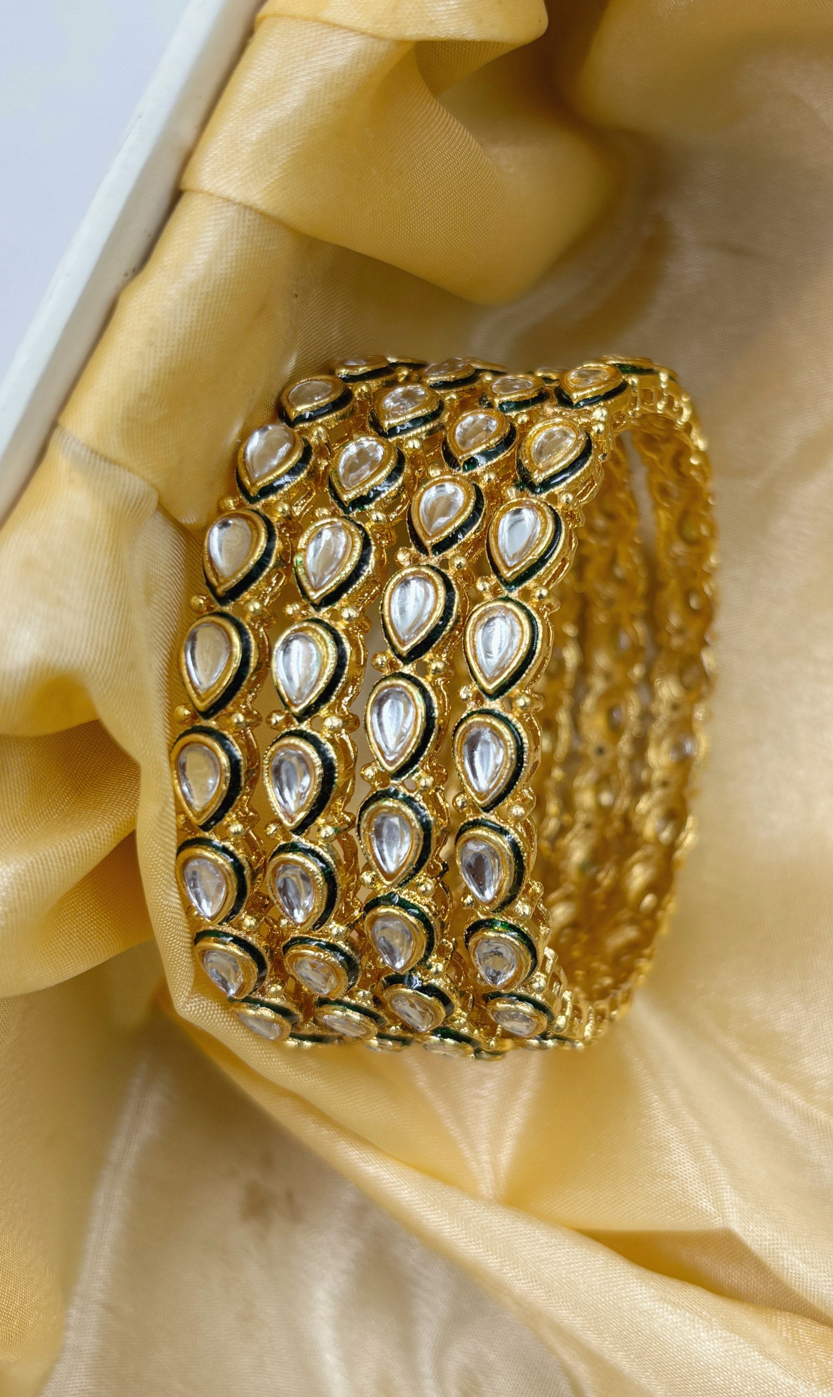 Set of gold bangles on a decorative stand with a patterned box in the background by hitesh bangles