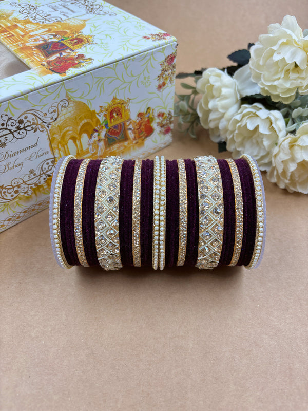 Wine velvet bridal bangle set featuring intricate gold-toned stonework and pearl detailing, displayed beside a decorative wedding-themed box and white artificial flowers on a brown background.