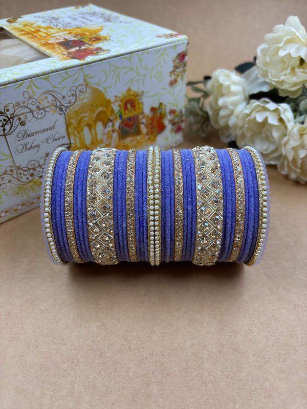 Pista green velvet bridal bangle set adorned with intricate gold-toned stonework and pearl detailing, displayed beside a decorative wedding-themed box and white artificial flowers on a brown background.









Pista green velvet bridal bangle set adorned with intricate gold-toned stonework and pearl detailing, displayed beside a decorative wedding-themed box and white artificial flowers on a brown background.









Purple velvet bridal bangle set adorned with intricate gold-toned stonework and pea