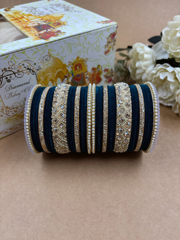 Navy blue velvet bridal bangle set featuring intricate gold-toned stonework and pearl accents, displayed alongside a decorative wedding box and white artificial flowers on a brown background.