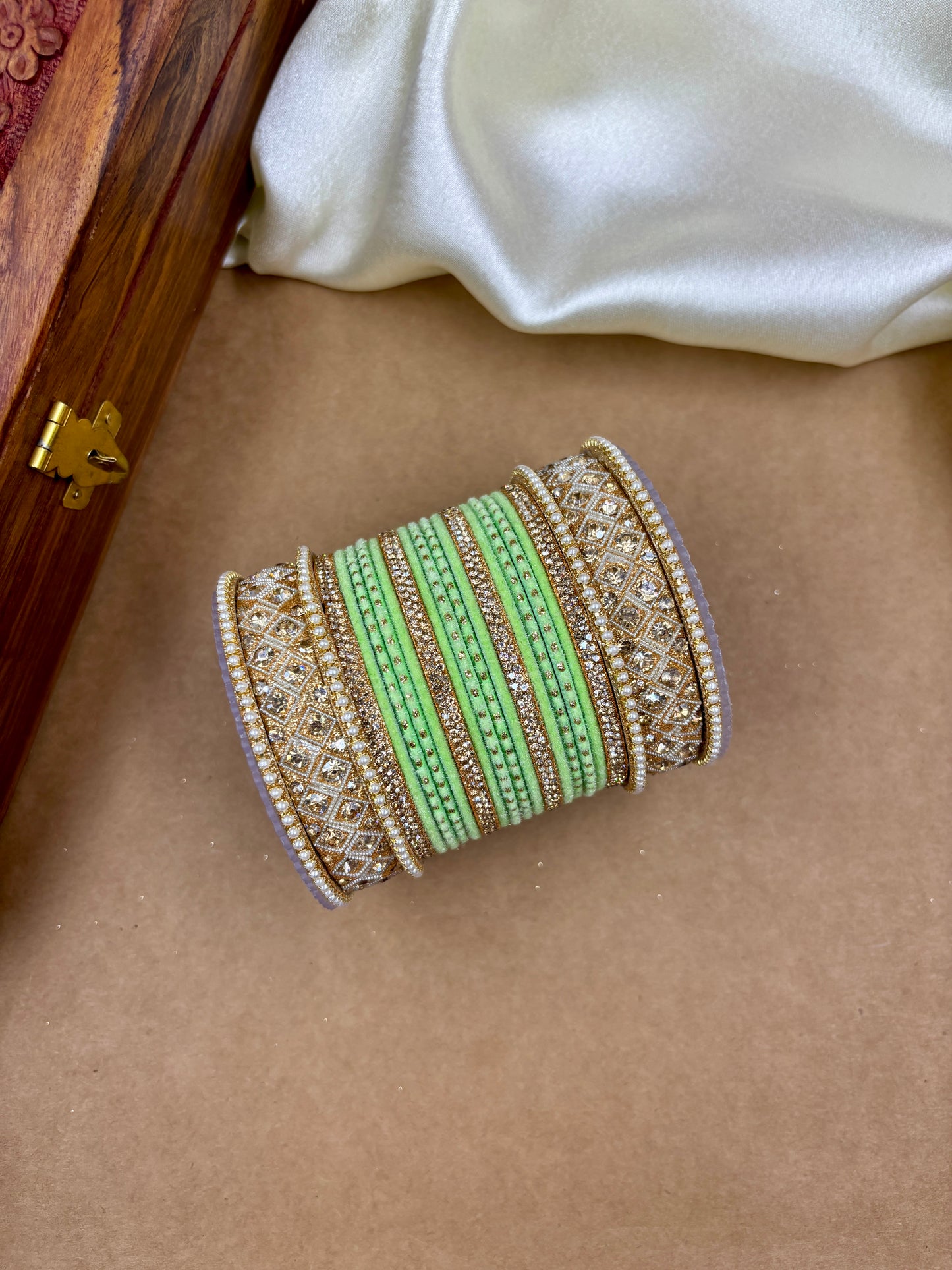 Decorative bangle with green and gold patterns on a brown surface by hitesh bangles