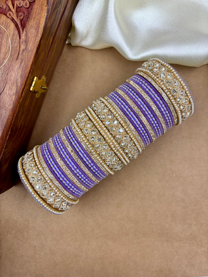 Lavender velvet bridal chooda set for women with gold-toned diamond-studded bangles, placed beside a wooden jewelry box and white satin fabric – perfect for Indian weddings and festive wear.