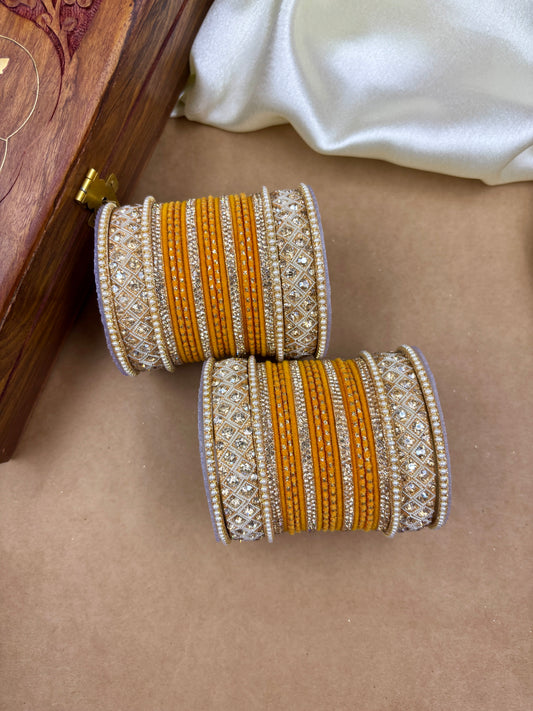Pair of ornate bangles with orange and silver design on a beige surface by hitesh bangles