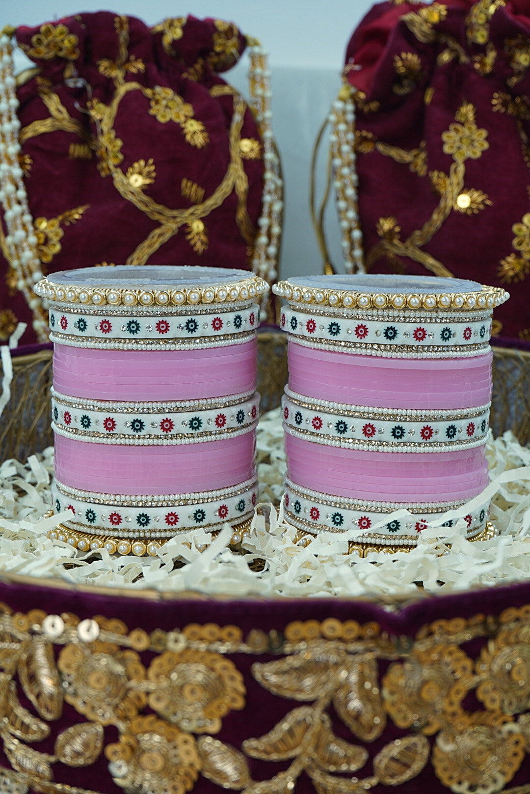 Two pink bangles with decorative patterns on a gold and maroon fabric background by hitesh bangles