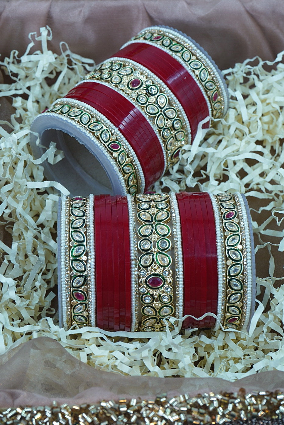 Decorative red bangles with gold patterns on a textured surface by hitesh bangles