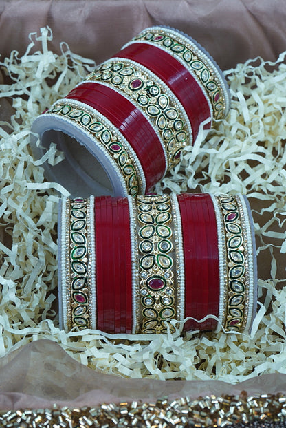 Decorative red bangles with gold patterns on a textured surface by hitesh bangles