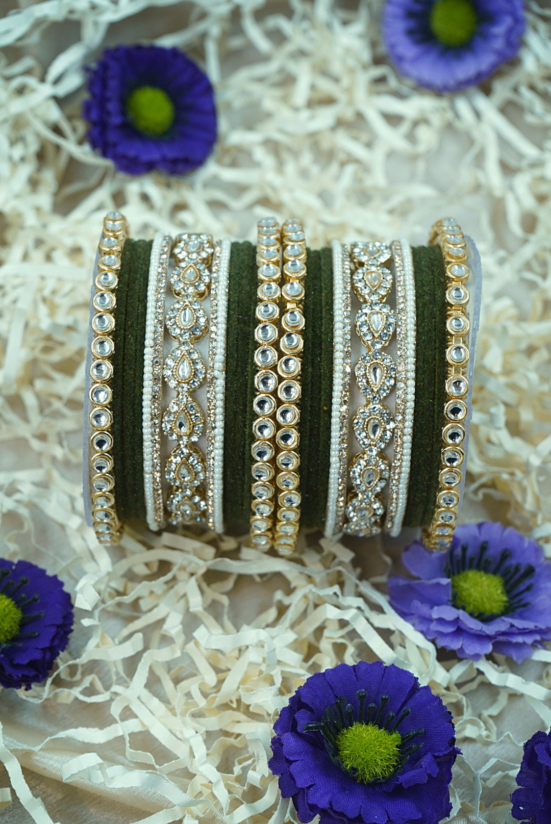 Decorative bangles with intricate designs on a textured surface with purple flowers by hitesh bangles