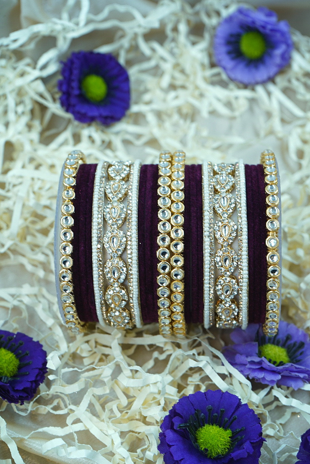 Set of decorative bangles with purple flowers on a textured white background by hitesh bangles
