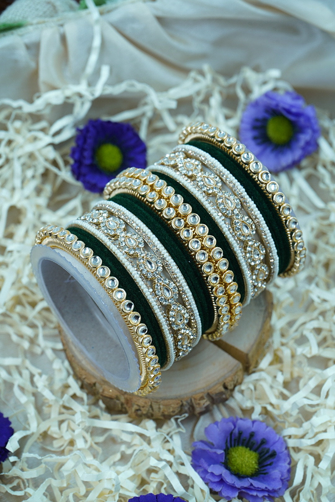 Set of gold and green bangles on a decorative stand with purple flowers in the background by hitesh bangles