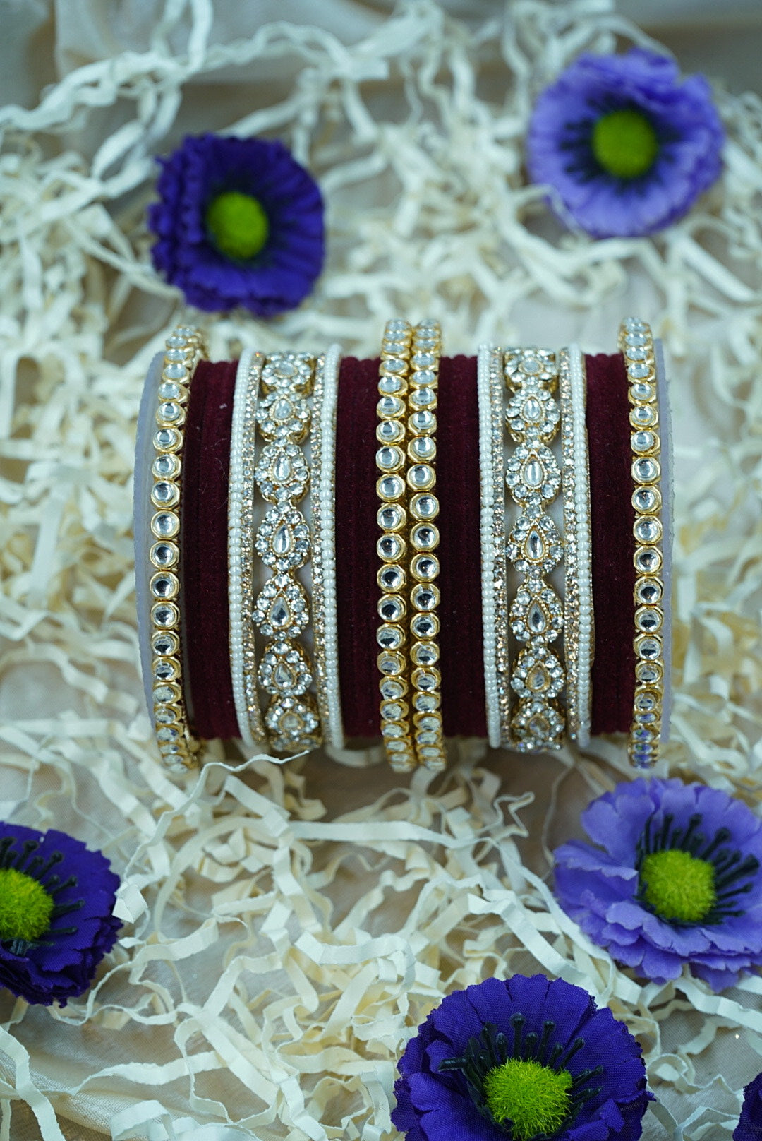Decorative bangles with intricate designs on a textured white surface with purple flowers by hitesh bangles