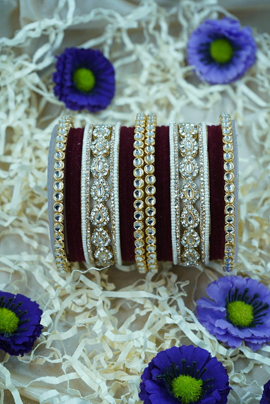 Decorative bangles with intricate designs on a textured white surface with purple flowers by hitesh bangles
