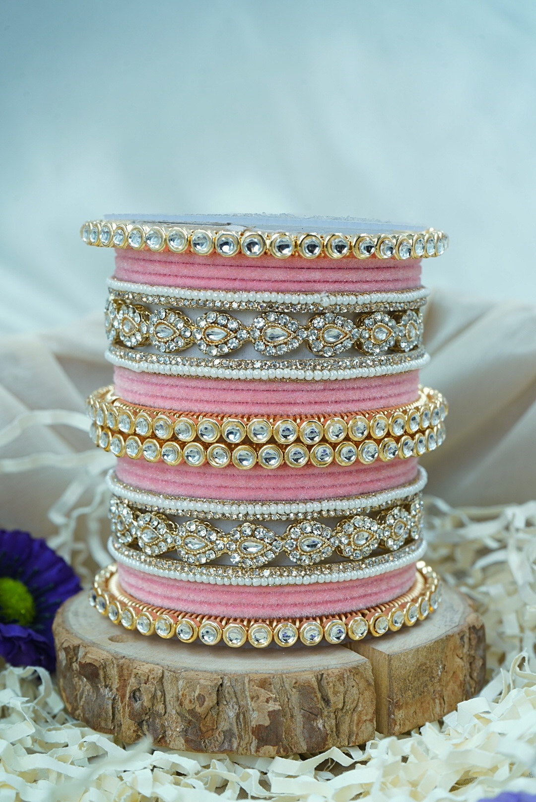 Stack of pink and gold bangles on a wooden stand with a white background by hitesh bangles