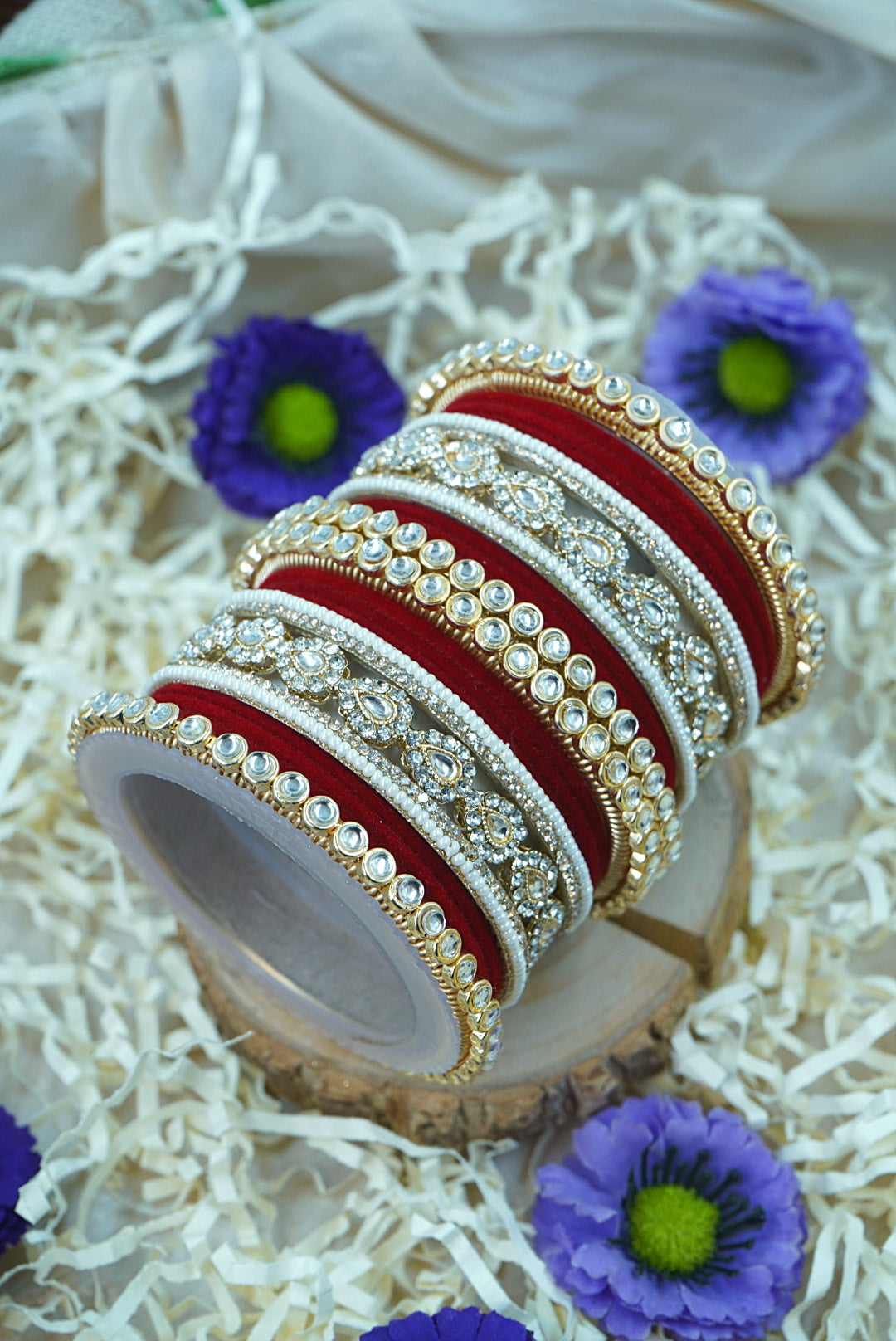 Decorative bangles with gold and red design on a white surface with purple flowers by hitesh bangles